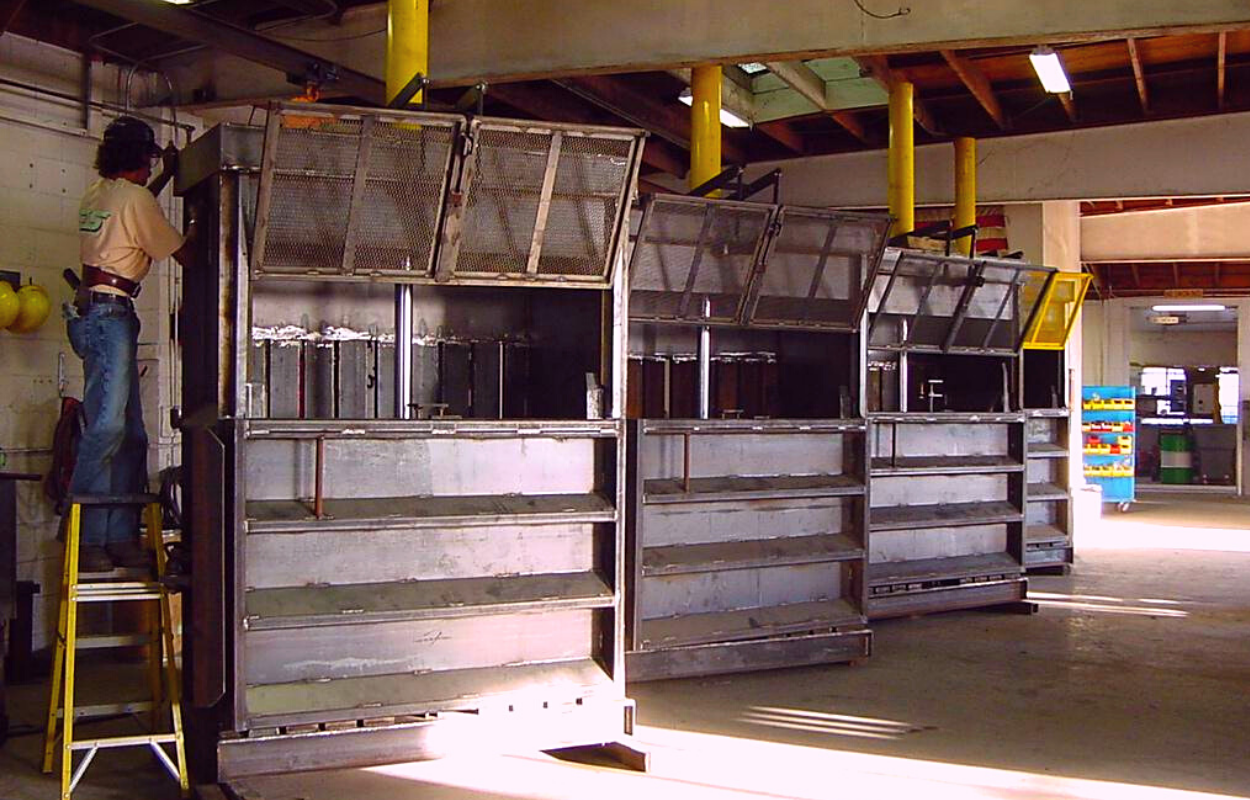 a worker repairing the first in a row of steel gray vertical balers pictured inside a factory