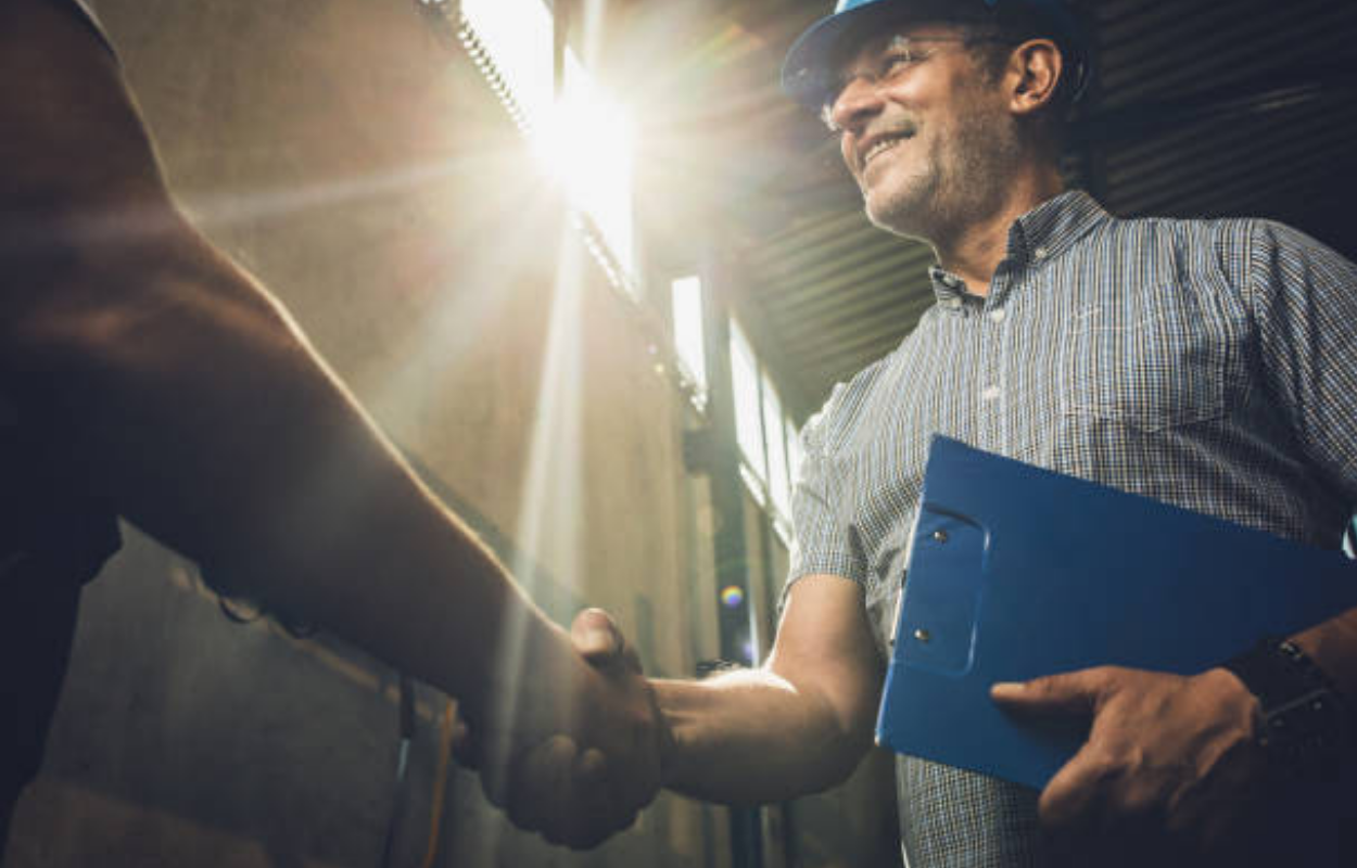 Low angle view of happy mid adult manager greeting unrecognizable person in a factory.