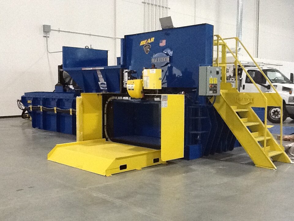 a blue horizontal recycling baler pictured with yellow stairs leading up to the top of the baler